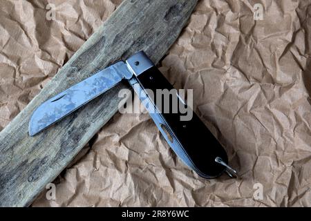 Treibholz mit altem, schwarzem, offenem Stiftmesser auf einer zerknitterten braunen Papieroberfläche Stockfoto
