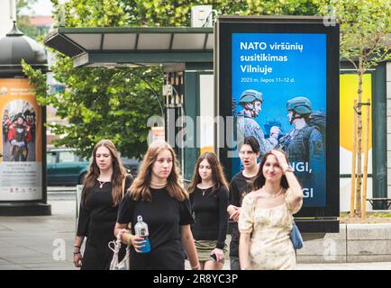 Ein Werbebanner informiert über den bevorstehenden NATO-Gipfel 2023 im Zentrum von Vilnius, der Hauptstadt Litauens, mit Teenagern, die zu Fuß unterwegs sind Stockfoto