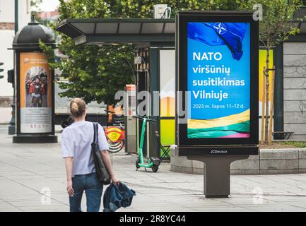 Werbebanner mit Informationen über den bevorstehenden NATO-Gipfel 2023 im Zentrum von Vilnius, der Hauptstadt Litauens, mit Mädchen, die in der Nähe spazieren gehen Stockfoto