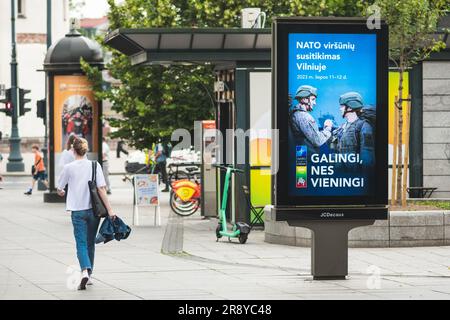 Werbebanner mit Informationen über den bevorstehenden NATO-Gipfel 2023 im Zentrum von Vilnius, der Hauptstadt Litauens, mit Mädchen, die in der Nähe spazieren gehen Stockfoto