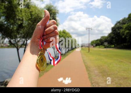 Verwischte Frauenhände, die Goldmedaillen mit thailändischem Band vor blauem Himmel halten, um Erfolg im Sport oder Geschäft zu zeigen, Gewinner erfolgreich Stockfoto