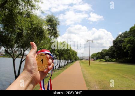 Verwischte Frauenhände, die Goldmedaillen mit thailändischem Band vor blauem Himmel halten, um Erfolg im Sport oder Geschäft zu zeigen, Gewinner erfolgreich Stockfoto