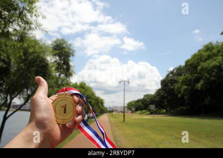 Verwischte Frauenhände, die Goldmedaillen mit thailändischem Band vor blauem Himmel halten, um Erfolg im Sport oder Geschäft zu zeigen, Gewinner erfolgreich Stockfoto