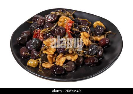 Gemischte schwarze Oliven. Spezielle gemischte Oliven, zubereitet mit getrocknetem roten Pfeffer, sonnengetrockneten Tomaten, Thymian, Walnüssen und Rosmarin, isoliert auf weißem Hintergrund. Stockfoto