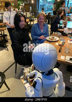 Tokio, Japan. 23. Juni 2023. Ein Roboter bringt Lisa Paus (Bündnis 90/die Grünen), Deutschlands Familienministerin, in einem innovativen Robotercafé in Tokio einen Espresso. Neben Paus sitzt der Chefentwickler Ory Yoshifuji. Kredit: Lars Nicolaysen/dpa/Alamy Live News Stockfoto