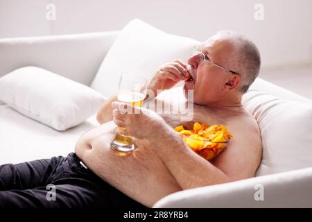 Übermäßiges Essen mit Junk Food, Bier trinken und Fernsehen Stockfoto