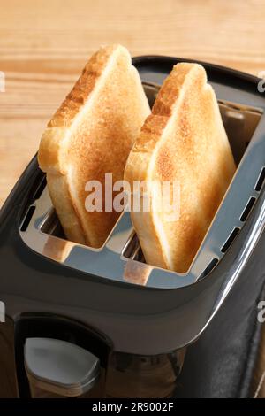 Nahaufnahme eines schwarz glänzenden Toasters mit braunem getoastetem Casinobrot zum Frühstück auf einem Holztisch. Stockfoto