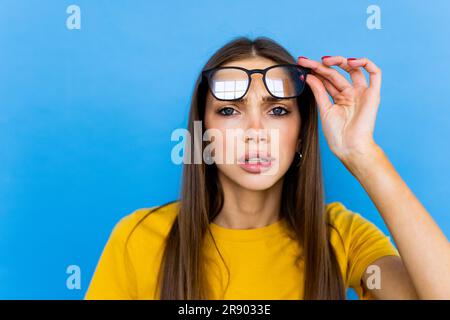 Foto von jungen asiatischen Mädchen erstaunt Schock gefälschte Neuheit Gerücht Hände berühren Brillen suchen leeren Raum isoliert über blauen Hintergrund Stockfoto