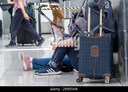München, Deutschland. 23. Juni 2023. Passagiere sitzen am Boden in der Abflughalle am Flughafen München und warten auf ihren Flug. Der Sturm über weite Teile Deutschlands hat auch den Flugverkehr beeinträchtigt. Zahlreiche Flugzeuge, die in München landen sollten, wurden umgeleitet. Kredit: Peter Kneffel/dpa/Alamy Live News Stockfoto