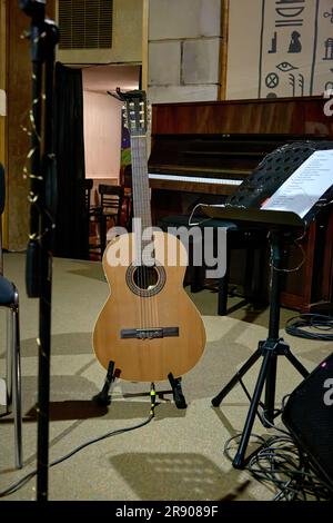 Das Bild einer Akustikgitarre steht auf der Bühne neben einem Musikstand Stockfoto