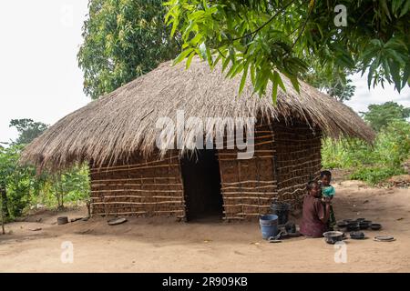 Eine alte Dame aus dem Makonde-Stamm sitzt in der primitiven Küche und bereitet lokale traditionelle Mahlzeit zu. Einfacher Metalltopf auf Feuer zwischen Steinen Stockfoto