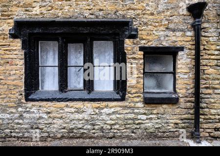 Alte Fensterrahmen und Regenwasserabflussrohre in einem alten Steinhaus in der Altstadt von Bourton on the Water, Cotswolds, Gloucestershire, England, United Stockfoto