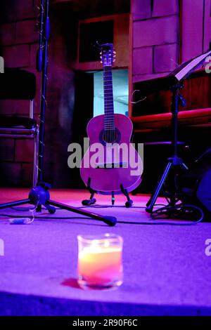 Das Bild einer Akustikgitarre steht auf der Bühne neben einem Musikstand Stockfoto