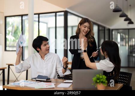 Erfolgreiche Geschäftsleute geben sich gegenseitig in einem Meeting ein High Five. Drei junge Unternehmen feiern Teamarbeit in einem Büro Stockfoto