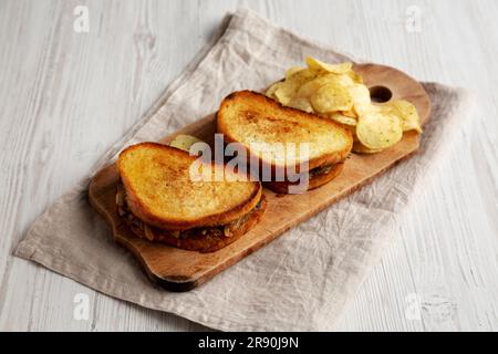 Hausgemachtes französisches Schmelzsandwich mit karamellisierten Zwiebeln und Gruyure-Käse auf einem rustikalen Holzbrett, Seitenblick. Stockfoto