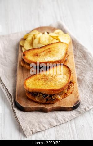 Hausgemachtes französisches Schmelzsandwich mit karamellisierten Zwiebeln und Gruyure-Käse auf einem rustikalen Holzbrett, Seitenblick. Stockfoto