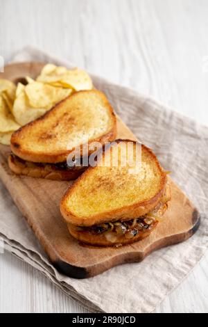 Hausgemachtes französisches Schmelzsandwich mit karamellisierten Zwiebeln und Gruyure-Käse auf einem rustikalen Holzbrett, Seitenblick. Speicherplatz kopieren. Stockfoto