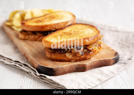 Hausgemachtes französisches Schmelzsandwich mit karamellisierten Zwiebeln und Gruyure-Käse auf einem rustikalen Holzbrett, Seitenblick. Nahaufnahme. Stockfoto