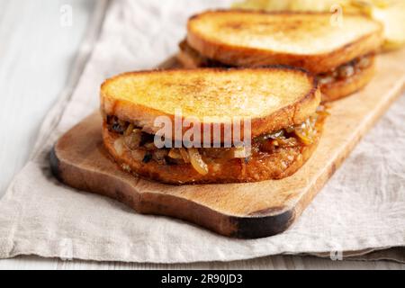 Hausgemachtes französisches Schmelzsandwich mit karamellisierten Zwiebeln und Gruyure-Käse auf einem rustikalen Holzbrett, Seitenblick. Nahaufnahme. Stockfoto