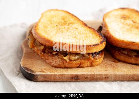 Hausgemachtes französisches Schmelzsandwich mit karamellisierten Zwiebeln und Gruyure-Käse auf einem rustikalen Holzbrett, Seitenblick. Nahaufnahme. Stockfoto