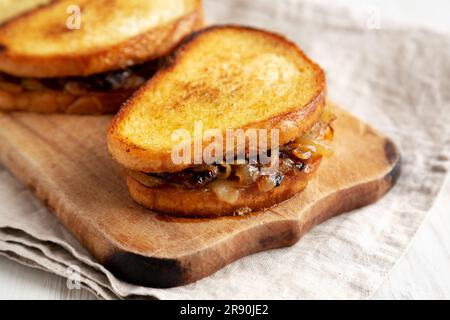 Hausgemachtes französisches Schmelzsandwich mit karamellisierten Zwiebeln und Gruyure-Käse auf einem rustikalen Holzbrett, Seitenblick. Nahaufnahme. Stockfoto