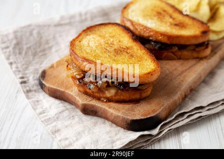 Hausgemachtes französisches Schmelzsandwich mit karamellisierten Zwiebeln und Gruyure-Käse auf einem rustikalen Holzbrett, Seitenblick. Nahaufnahme. Stockfoto