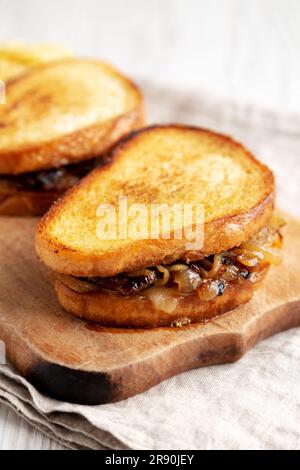 Hausgemachtes französisches Schmelzsandwich mit karamellisierten Zwiebeln und Gruyure-Käse auf einem rustikalen Holzbrett, Seitenblick. Nahaufnahme. Stockfoto