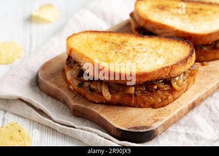 Hausgemachtes französisches Schmelzsandwich mit karamellisierten Zwiebeln und Gruyure-Käse auf einem rustikalen Holzbrett, Seitenblick. Nahaufnahme. Stockfoto