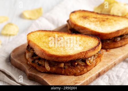 Hausgemachtes französisches Schmelzsandwich mit karamellisierten Zwiebeln und Gruyure-Käse auf einem rustikalen Holzbrett, Seitenblick. Stockfoto