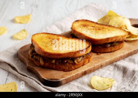 Hausgemachtes französisches Schmelzsandwich mit karamellisierten Zwiebeln und Gruyure-Käse auf einem rustikalen Holzbrett, Seitenblick. Stockfoto