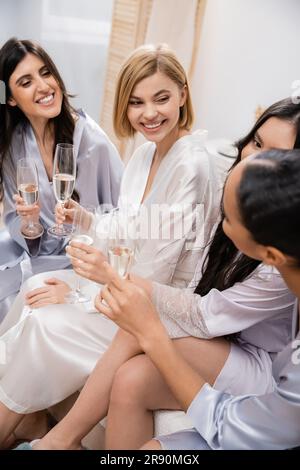 hochzeitsfeier, gemischtrassige Freundinnen, die Gläser mit Champagner halten, Feier vor der Hochzeit, brünette und blonde Frauen, glückliche Braut und Brautjungfer Stockfoto