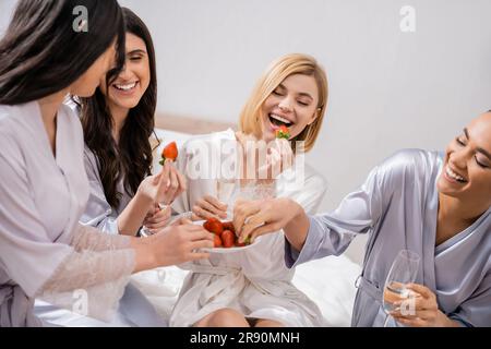 Erdbeeren und Champagner, Gelächter, vier Frauen, Hochzeitsfeier, gemischtrassige Freundinnen, die Spaß haben, brünett und blond, Braut und ihre Brautjungfern spe Stockfoto