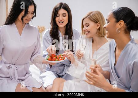 Erdbeeren und Champagner, vier Frauen, Brautparty, gemischtrassige Freundinnen, die Spaß haben, brünett und blond, Braut und Brautjungfern, die Zeit verbringen Stockfoto