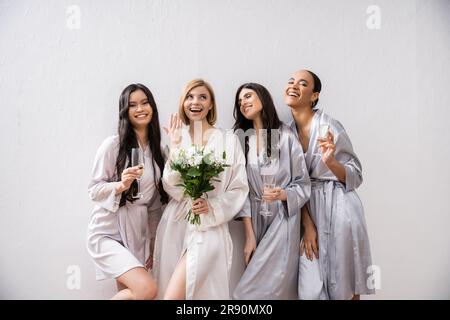 hochzeitsfeier, multikulturelle Frauen, die Gläser mit Champagner halten, Braut mit weißen Blumen, die ihren Verlobungsring zeigt, Brautjungfern, Vielfalt, Positi Stockfoto