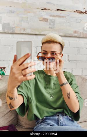 Online-Internet-Tausch, bewusste Entschlüsselung, junge tätowierte Frau mit trendigen Haaren nimmt Selfie in modischer Sonnenbrille auf Smartphone, Sustai Stockfoto