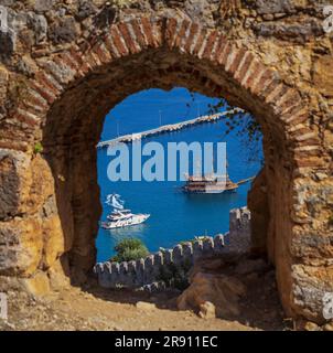 Blick auf touristische Schiffe durch den Bogen einer Steinfestung in Alanya. Stockfoto