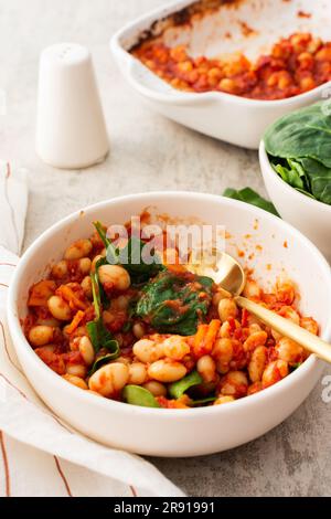 Gesundes Frühstück und Mittagessen, gedünstete weiße Bohnen mit Karotten, Zwiebeln und Tomaten mit Spinatblättern, eine Schüssel Bohnen und Spinat Stockfoto