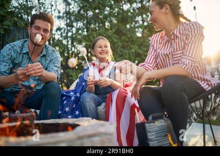 Die Familie versammelt sich in ihrem Hinterhof und sonnt sich in der Freude der Zusammengehörigkeit. Die Eltern und ihre Tochter werden dabei gesehen, wie sie sich mit dem einfachen Vergnügen von Roas verwöhnen lassen Stockfoto