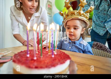 Ein junges Mädchen strahlt pure Freude aus, wenn sie ihren besonderen Tag in Gesellschaft ihrer liebevollen Eltern feiert. Vor einem herrlichen Geburtstagskuchen. Stockfoto