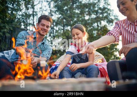 Die Familie versammelt sich in ihrem Hinterhof und sonnt sich in der Freude der Zusammengehörigkeit. Die Eltern und ihre Tochter werden dabei gesehen, wie sie sich mit dem einfachen Vergnügen von Roas verwöhnen lassen Stockfoto