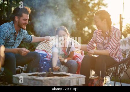 Die Familie versammelt sich in ihrem Hinterhof und sonnt sich in der Freude der Zusammengehörigkeit. Die Eltern und ihre Tochter werden dabei gesehen, wie sie sich mit dem einfachen Vergnügen von Roas verwöhnen lassen Stockfoto