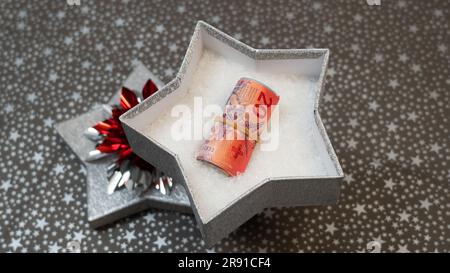 Möglichkeit, Geld zu spenden (schweizer Franken CHF) als Geschenk. Geld als Geschenk zu geben. Ein monetäres Geschenk in einer silbernen, glänzenden Sternenkiste, Sternenmuster, mehrfarbig, Regenbogen Stockfoto