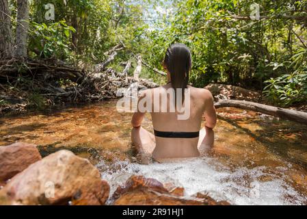 Eine Frau in einem Bikini hält sich in einem seichten Süßwasserstrom im Litchfield-Nationalpark in Australien kühl Stockfoto