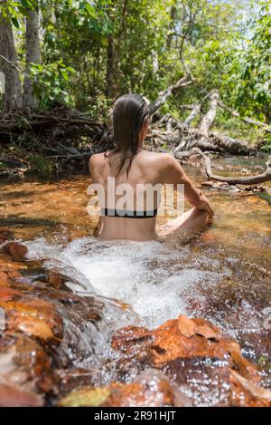 Eine Frau in einem Bikini hält sich in einem seichten Süßwasserstrom im Litchfield-Nationalpark in Australien kühl Stockfoto