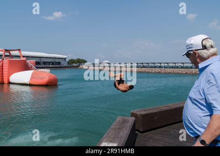 Ein Mann mit blauem Hemd sieht zu, wie ein junger Mensch von einer Mauer ins Meer springt, in Darwin in Australien Stockfoto