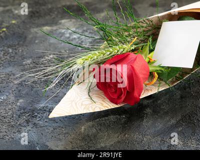Eine Nahaufnahme eines ästhetischen Blumenstraußes mit einer roten Rose und Weizen auf einem schwarzen Tisch Stockfoto