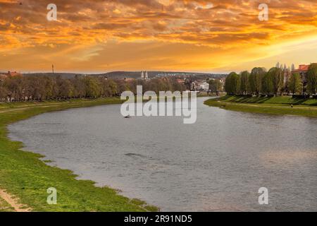 Dramatische Sonnenuntergangslandschaft über dem UZH-Fluss, die alte und moderne Stadt in Uschhorod, Ukraine, verbindet. Die Stadt hat ihren Namen vom UZH River. Stockfoto