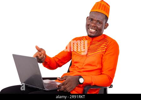 Ein gutaussehender Mann mit Hut zu Hause auf weißem Hintergrund, der auf den Laptop zeigt und lächelnd auf die Kamera schaut. Stockfoto