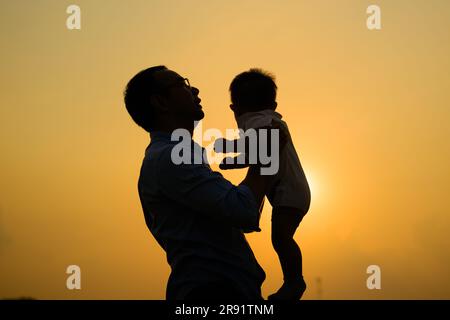 Glücklicher Vater hält das Neugeborene und spielt mit Blick auf den Sonnenuntergang Stockfoto