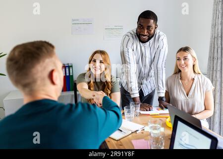 Lächelnde Geschäftsfrau und Geschäftsmann, die sich am Arbeitsplatz die Hand schütteln Stockfoto